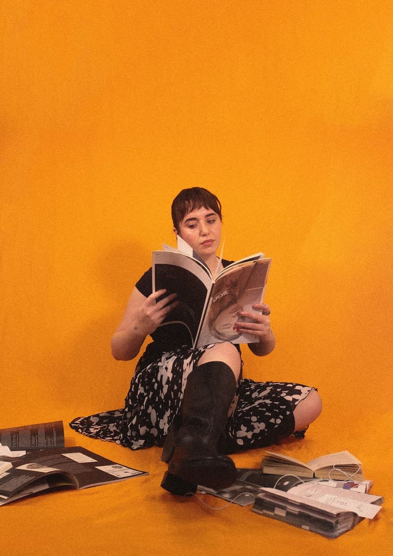 Fun headshot of Cleo sitting on the floor and reading a stack of design books.